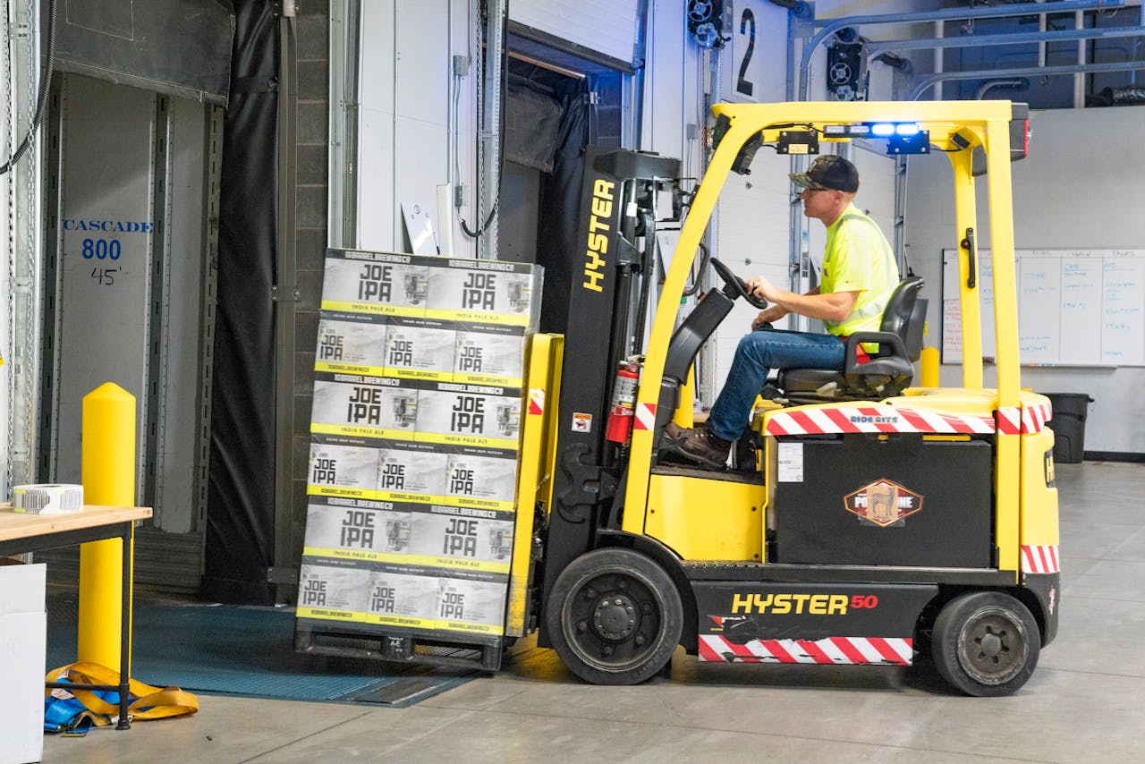 mobile-02 A worker drives a Hyster forklift moving Joe IPA boxes in a warehouse.