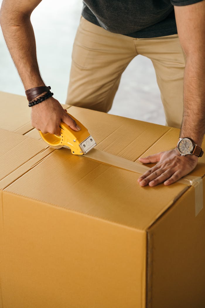 brand-01 Unrecognizable man sealing box with duck tape while preparing for moving out
