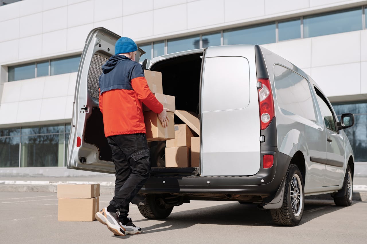brand-03 Man in colorful jacket loading cardboard boxes into a van outside an office building.