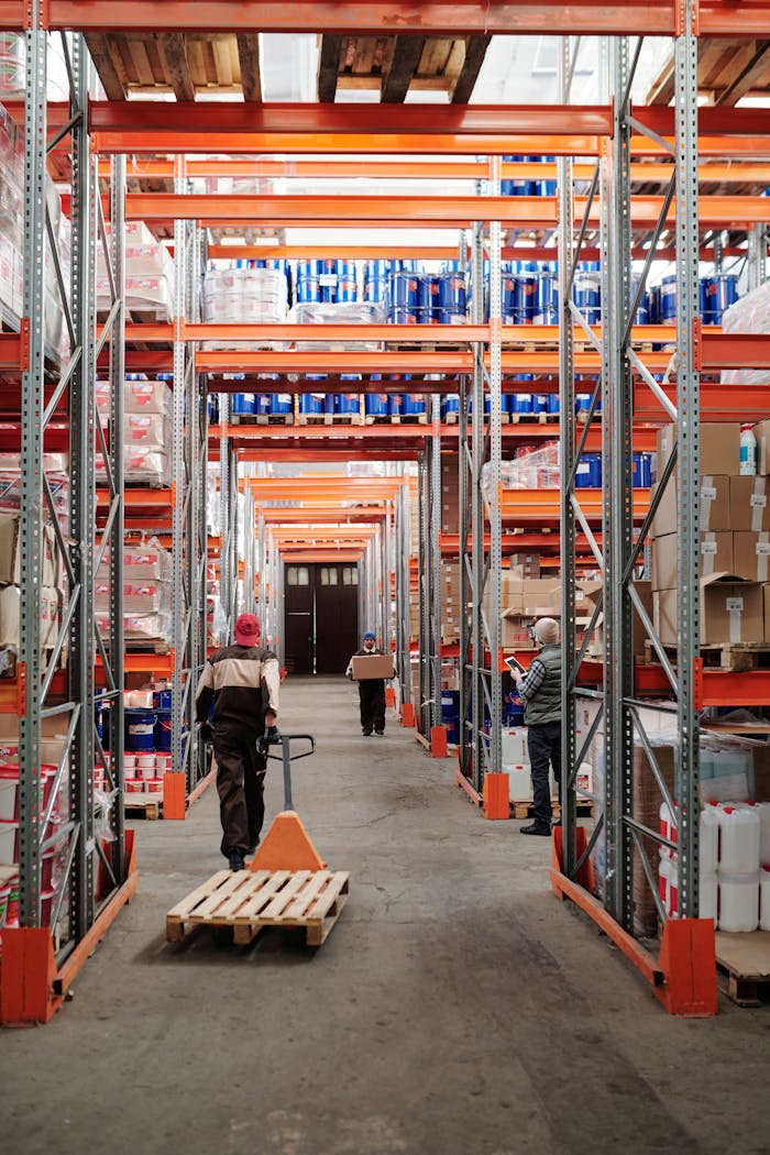 brand-02 Workers arrange inventory on shelves in a large industrial warehouse.