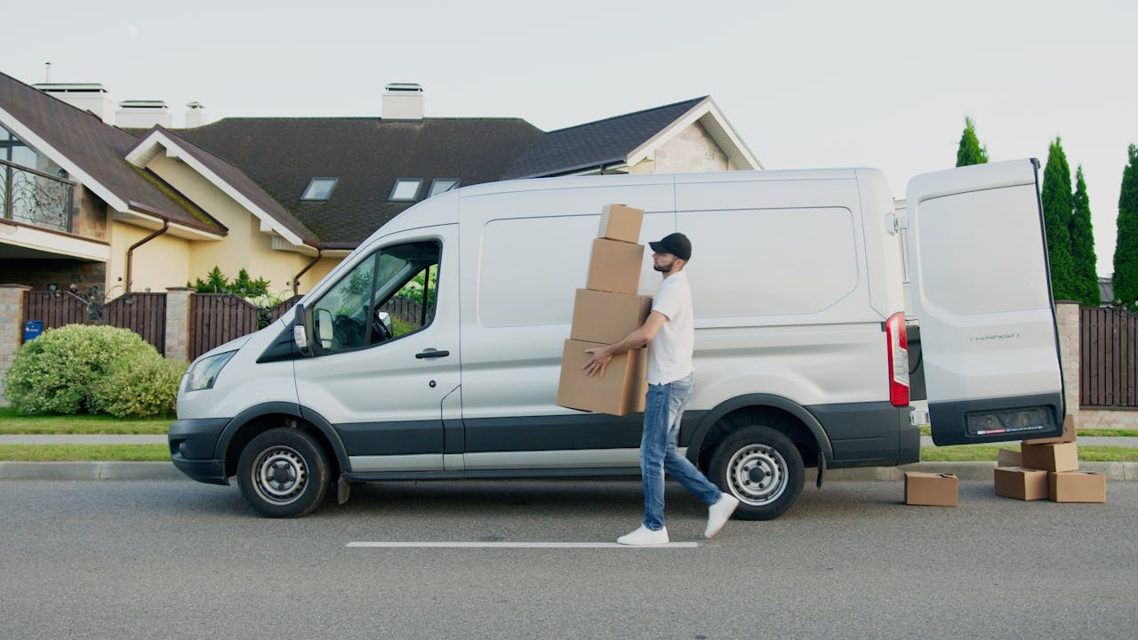 creative-03 Man unloading cardboard boxes from a delivery van in a suburban neighborhood street.
