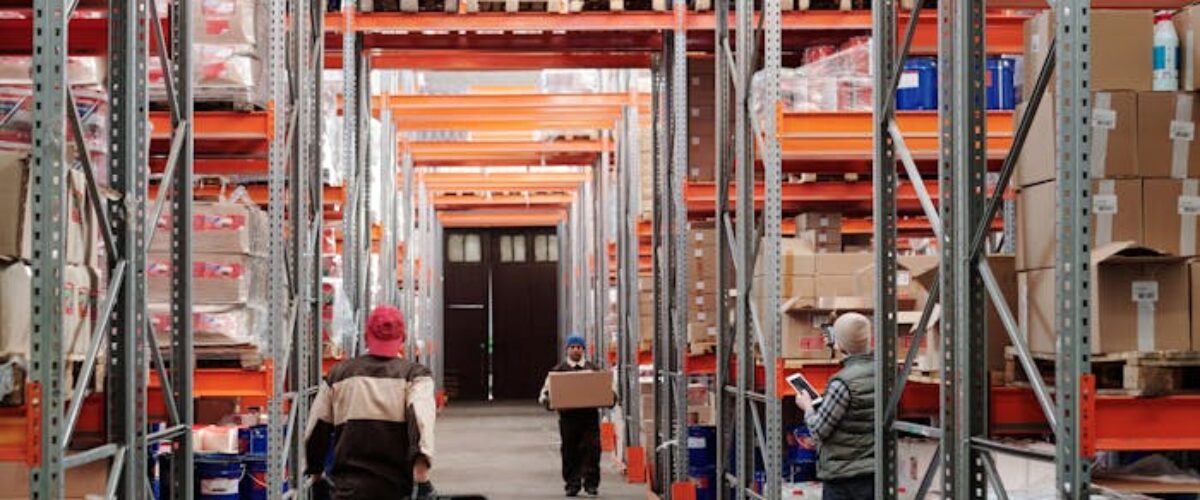 Workers arrange inventory on shelves in a large industrial warehouse.